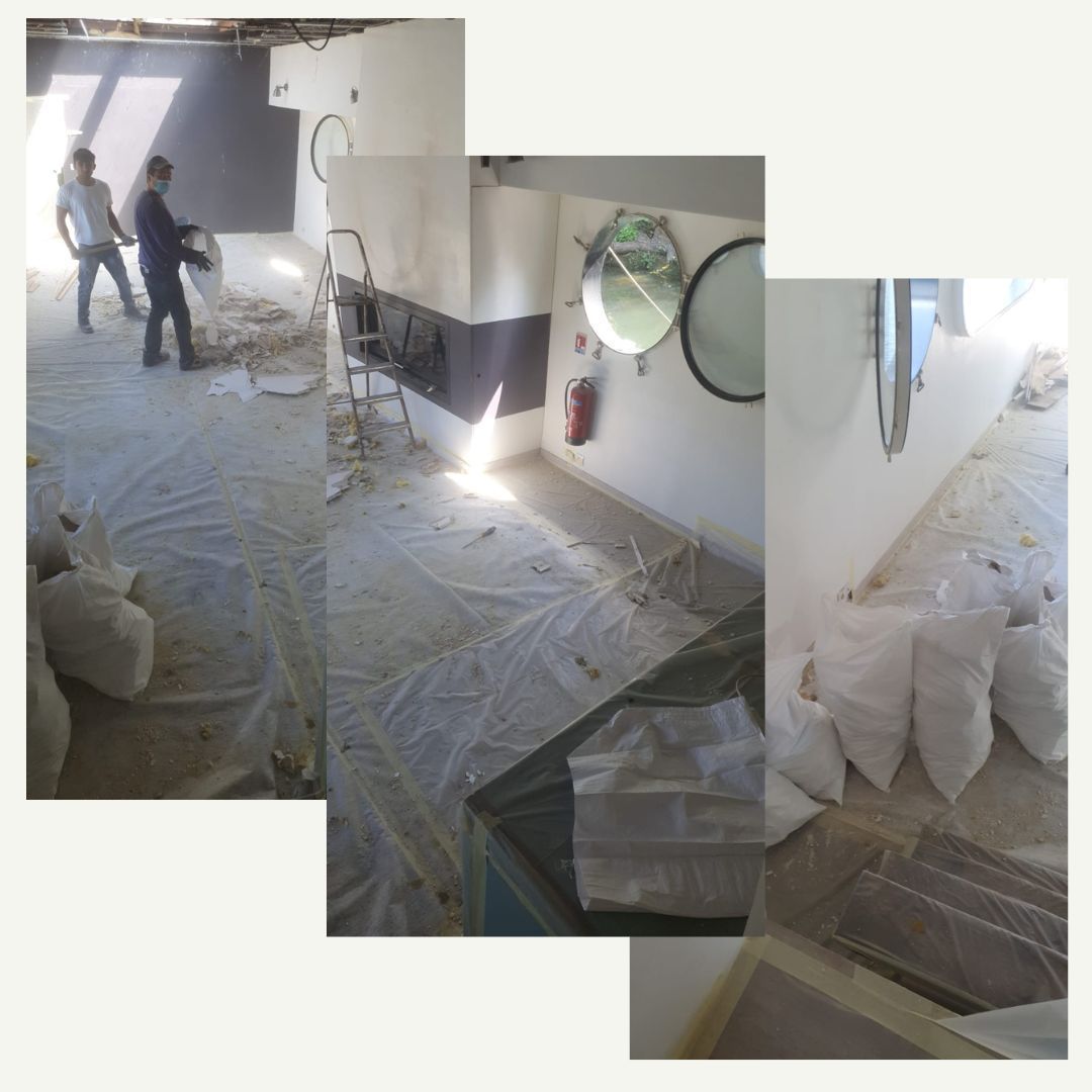 Rénovation en cours : ouvriers dans une pièce au sol recouvert, jonchée de débris, de sacs blancs et dotée d’un hublot.