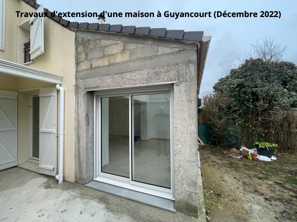 Travaux d'agrandissement d'une maison à Guyancourt : nouveaux murs en parpaings gris, porte coulissante en verre, inachevés.