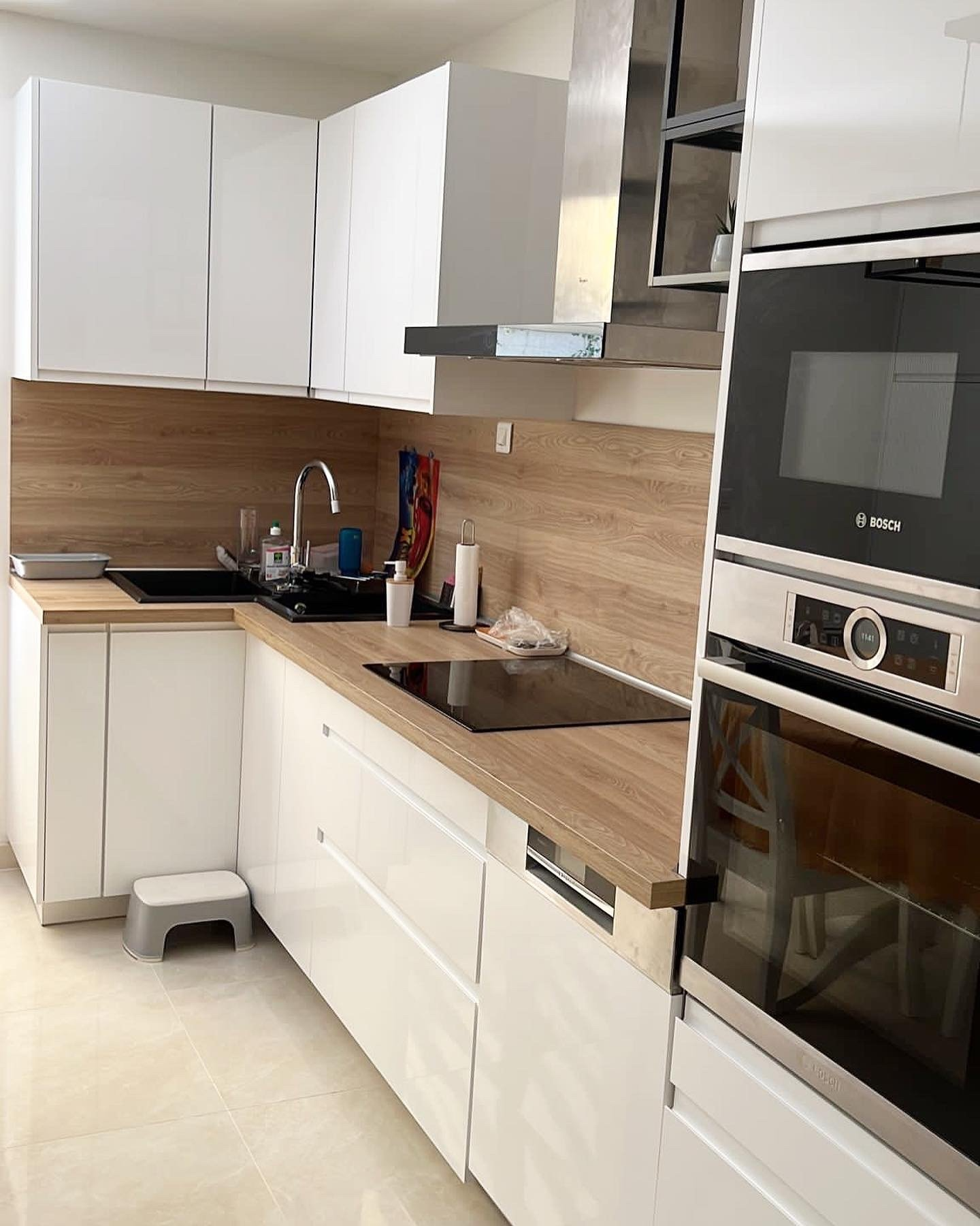 Cuisine moderne blanche avec comptoirs en bois, appareils électroménagers intégrés et hotte en acier inoxydable.