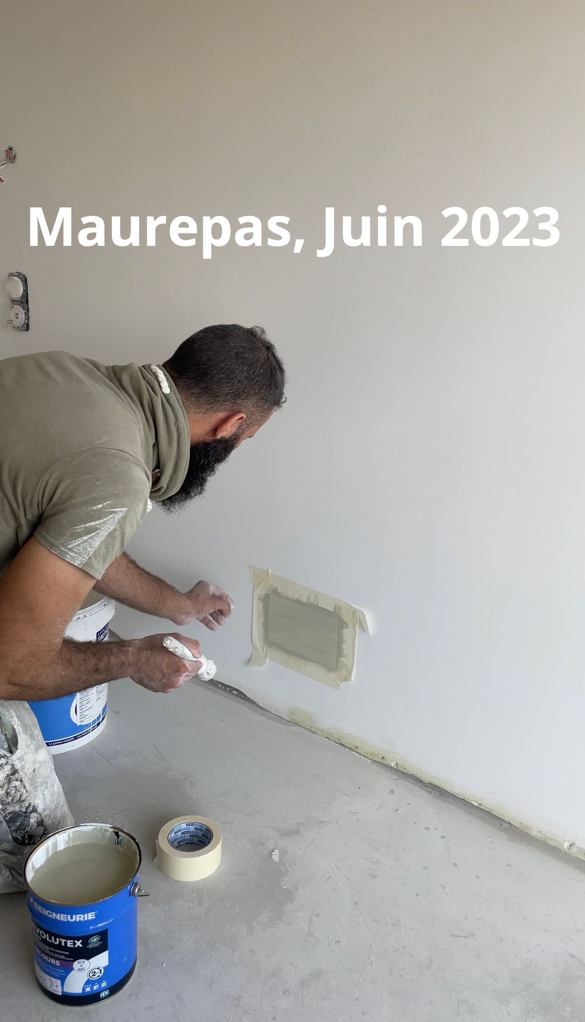 Personne appliquant du mastic autour d'un trou carré dans un mur blanc ; Maurepas, juin 2023.