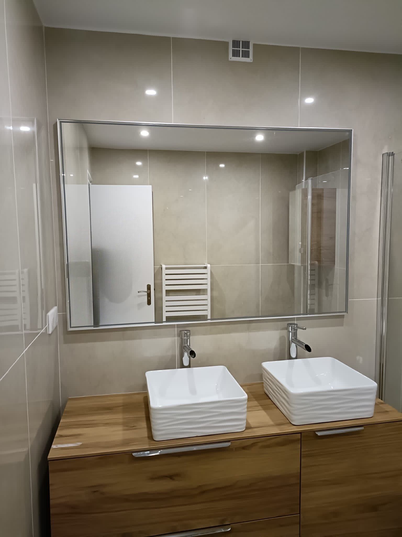 Salle de bains avec double vasque, grand miroir et meuble en bois. Murs carrelés beiges.