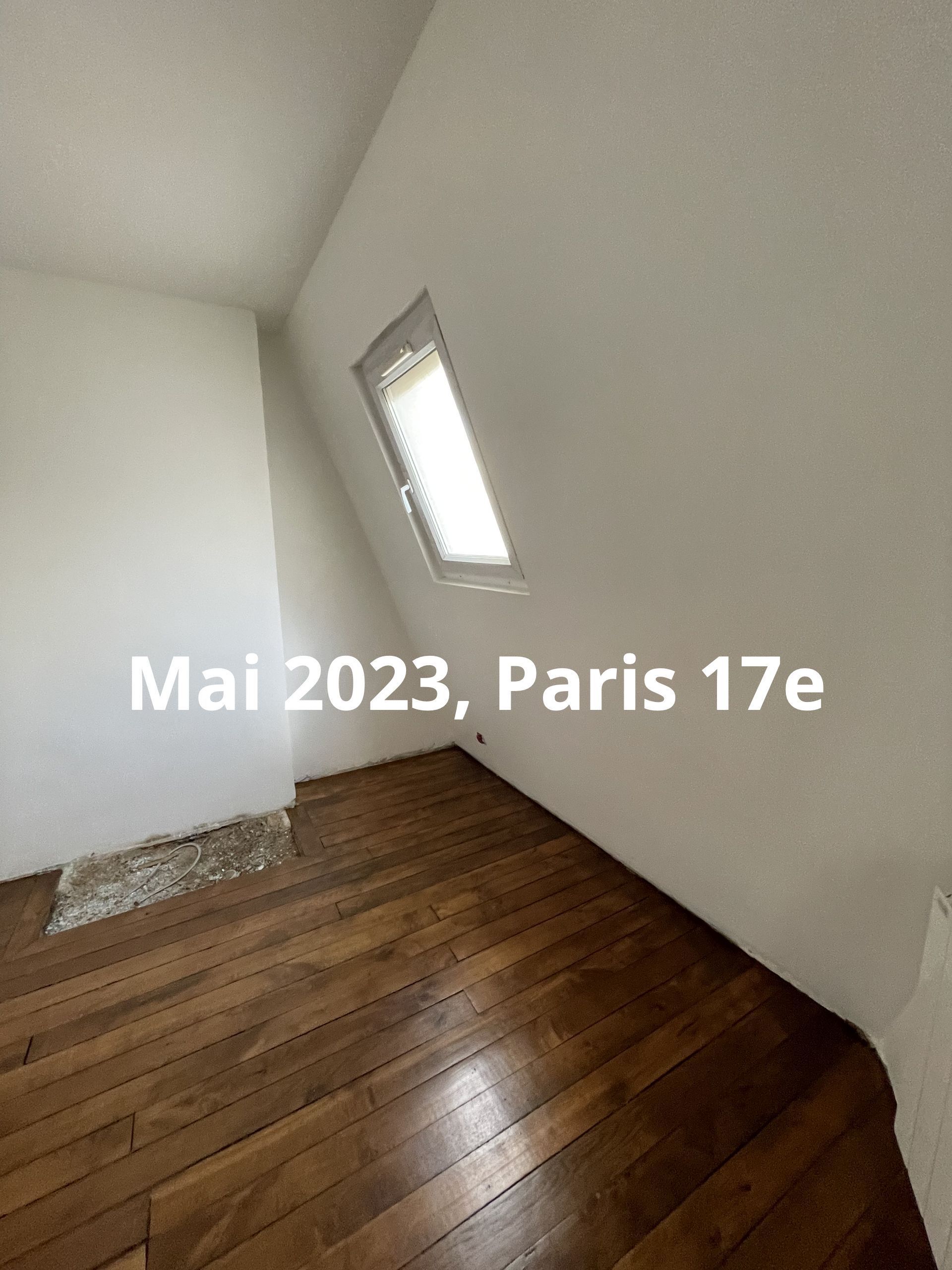 Pièce mansardée vide avec des murs blancs en pente, un plancher en bois et une petite fenêtre.