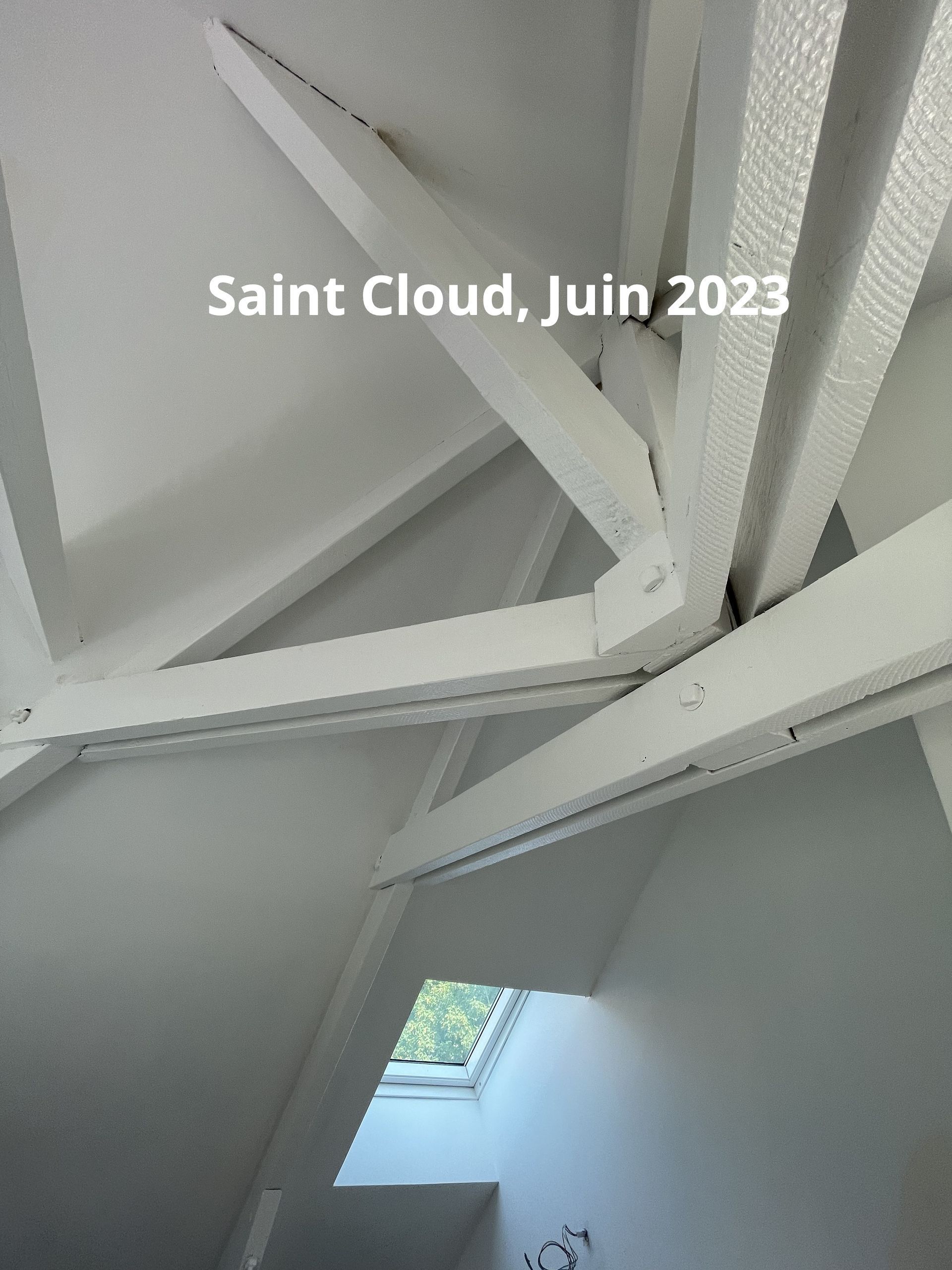 Poutres en bois peintes en blanc dans un grenier, avec un puits de lumière et le texte « Saint Cloud, juin 2023 ».