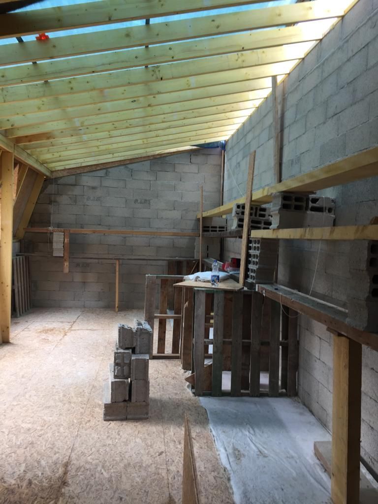 Intérieur d'un bâtiment partiellement construit, avec des murs en parpaings, un toit en bois et des palettes.