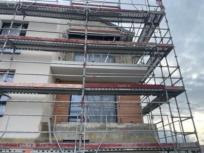 Extérieur du bâtiment avec échafaudages ; travaux de construction en cours sur une structure résidentielle.