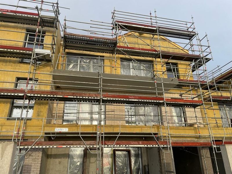 Extérieur du bâtiment en construction ; échafaudages, isolation jaune, fenêtres.