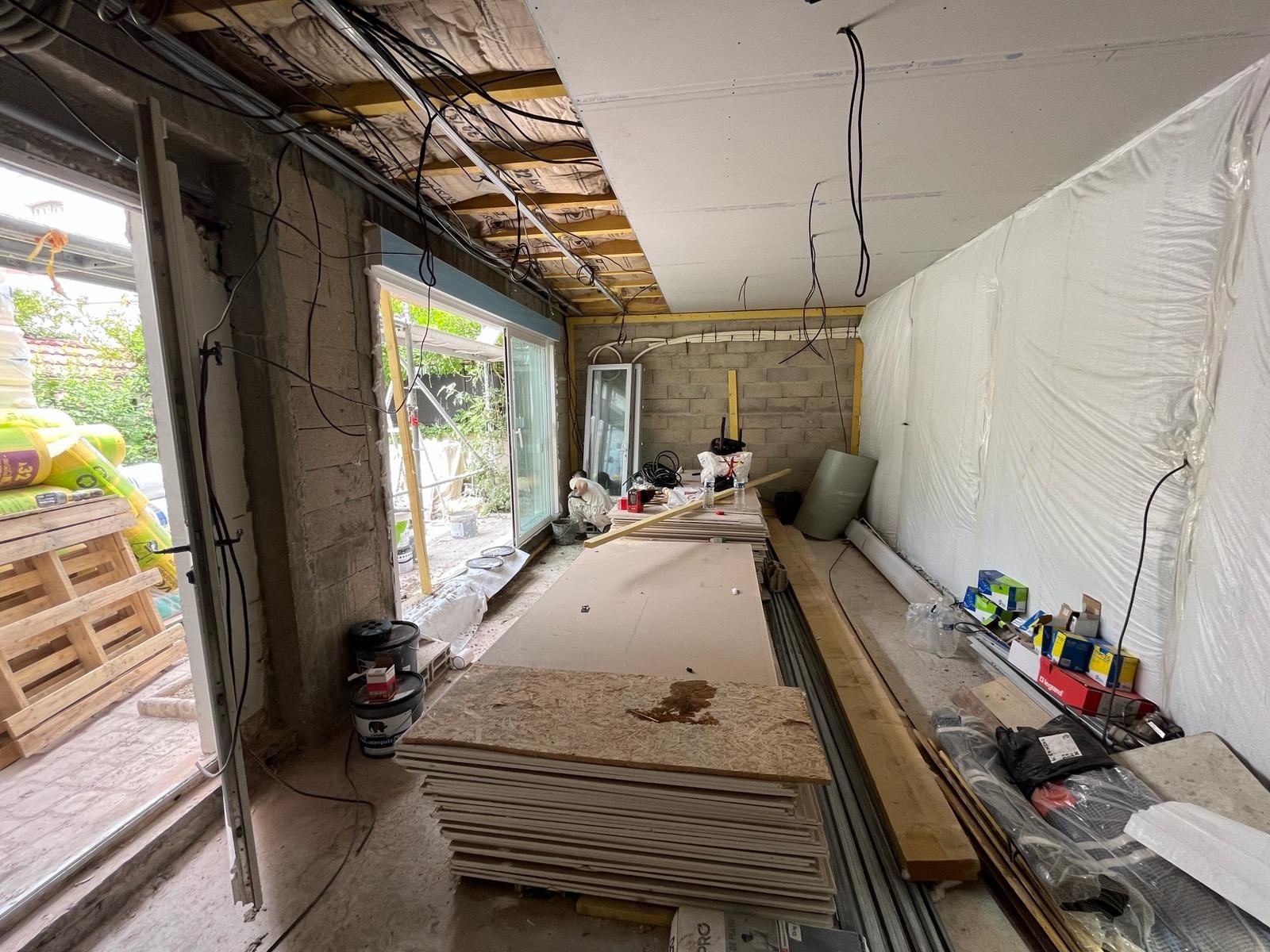 Pièce en travaux, avec poutres apparentes au plafond, cloisons sèches et une grande baie vitrée.