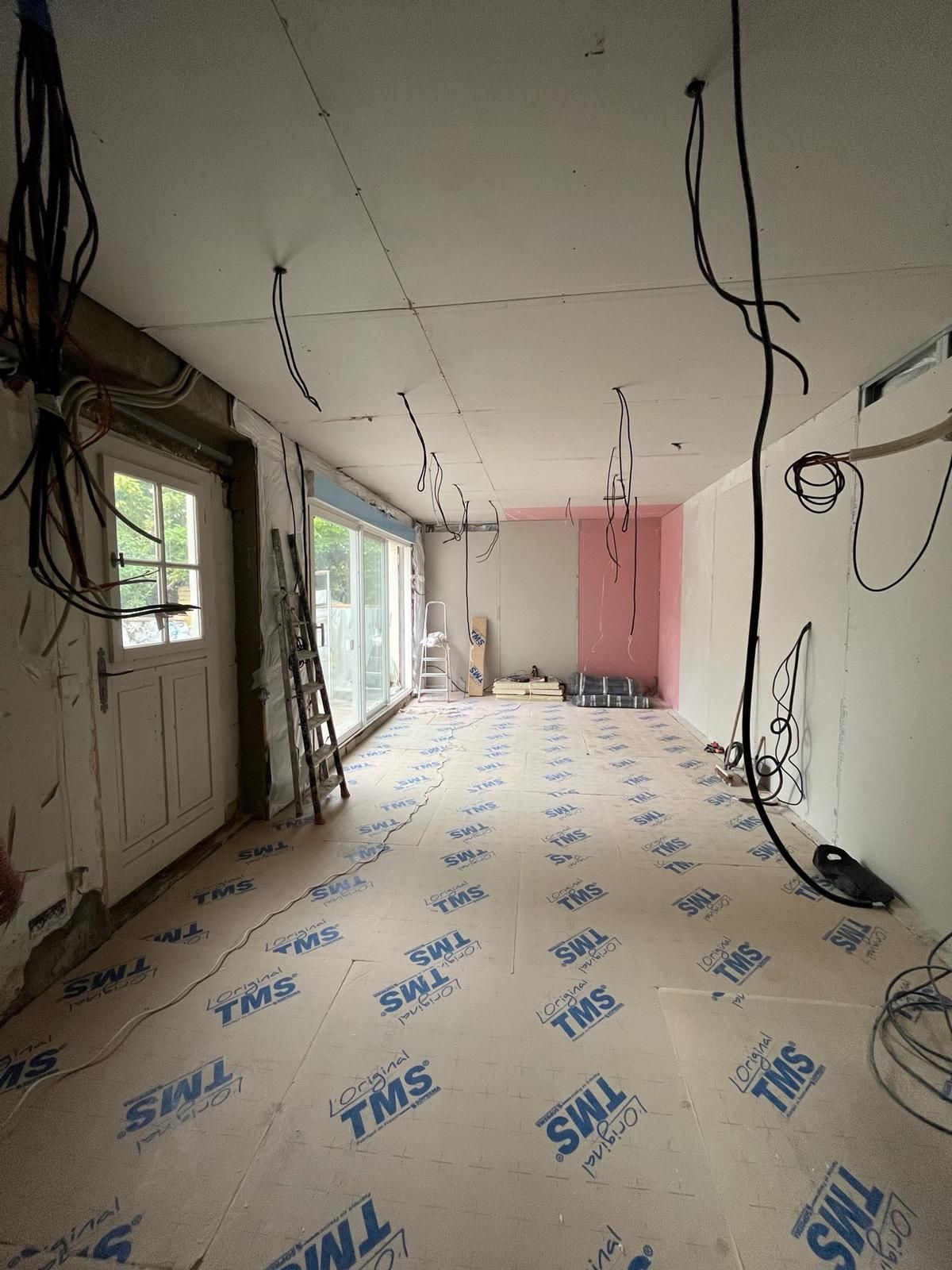 Pièce intérieure en construction, avec câblage apparent, isolation et revêtement de sol protecteur.