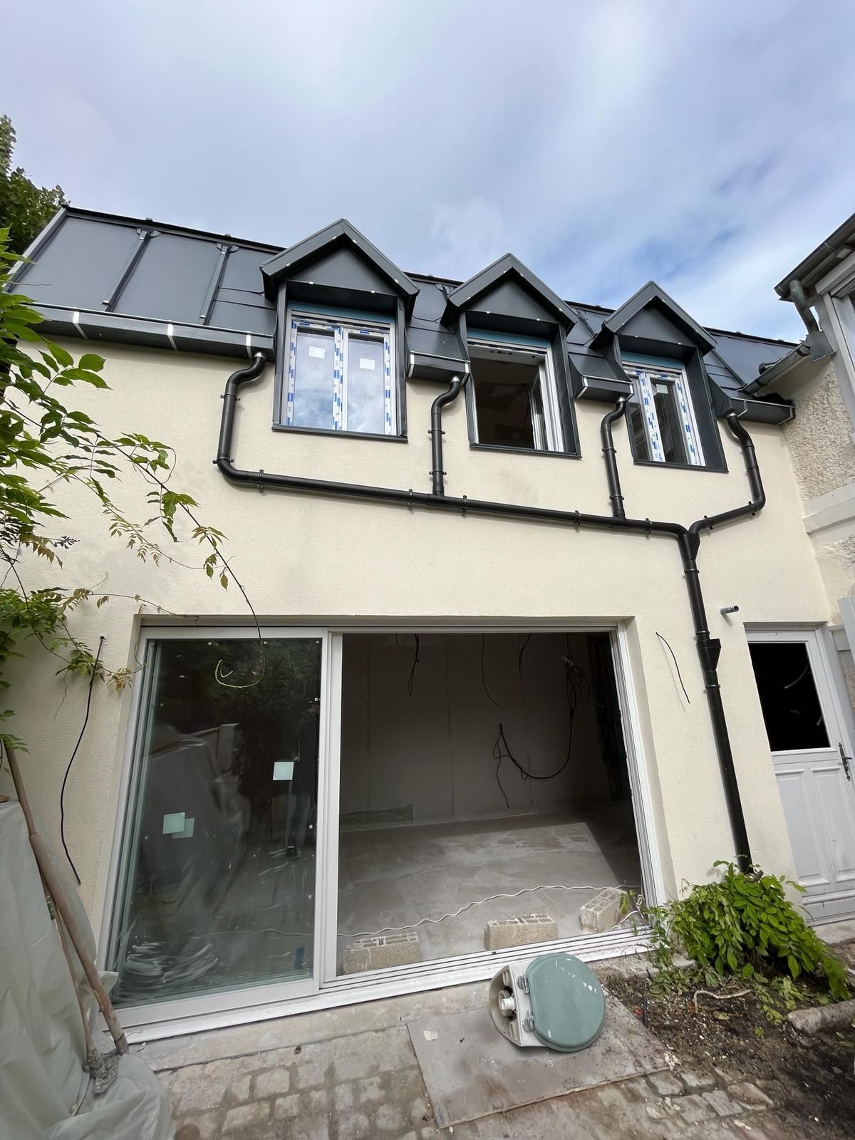 Extérieur du bâtiment avec portes coulissantes en verre, trois lucarnes et toit sombre.