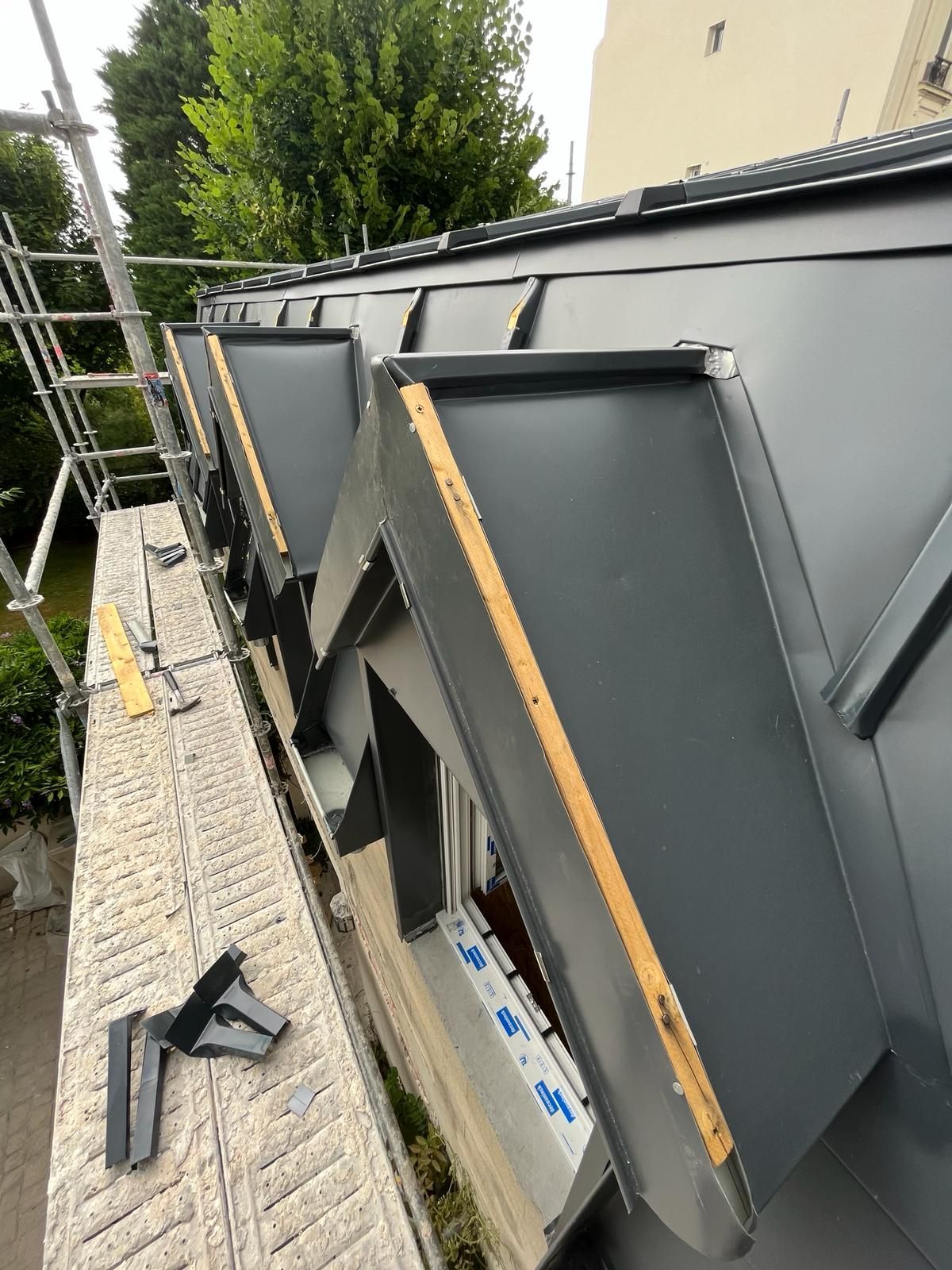 Toiture métallique grise avec lucarnes, vue depuis un échafaudage.