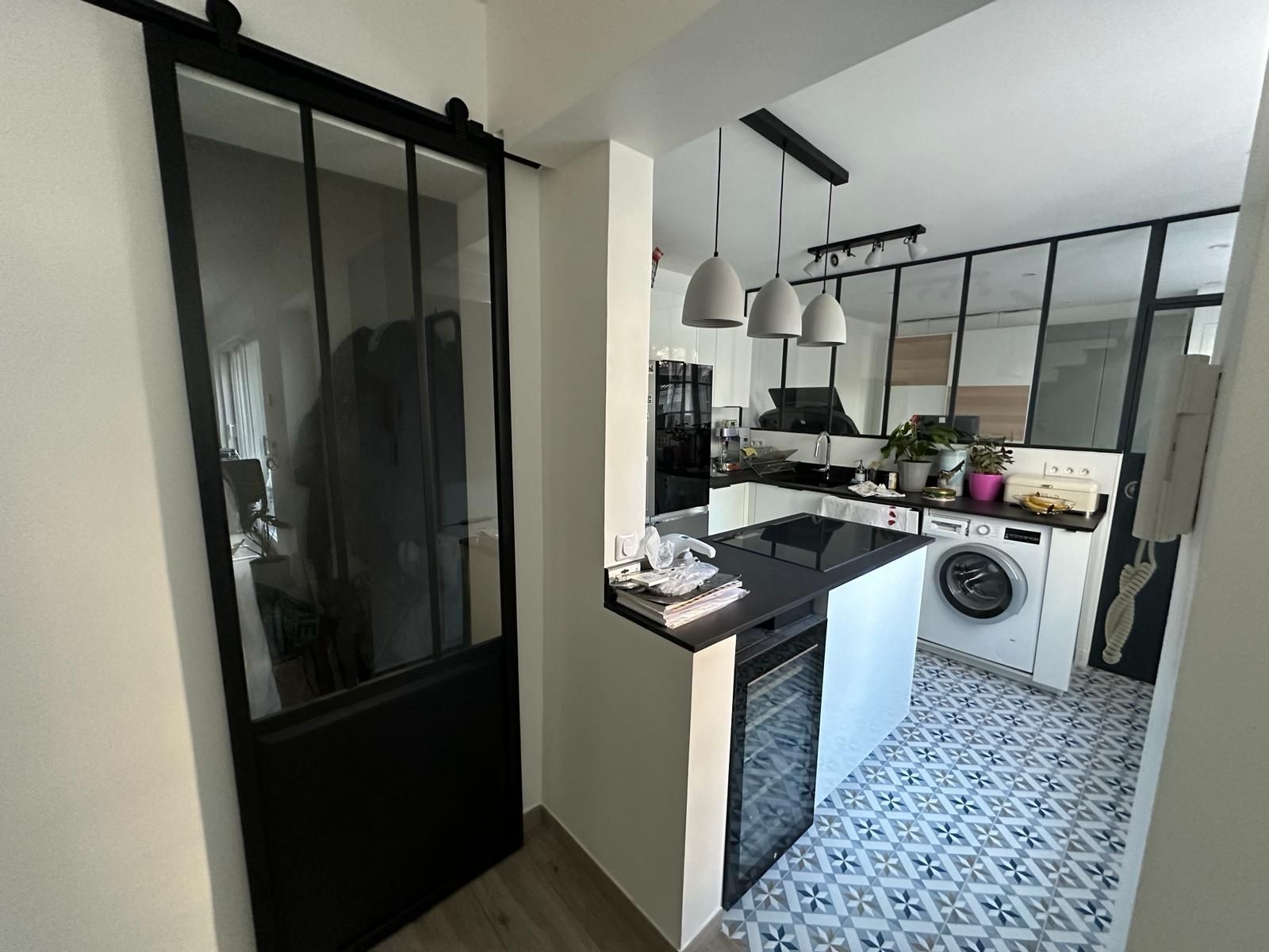 Porte coulissante en verre noir et cuisine avec sol carrelé de carreaux bleus à motifs.