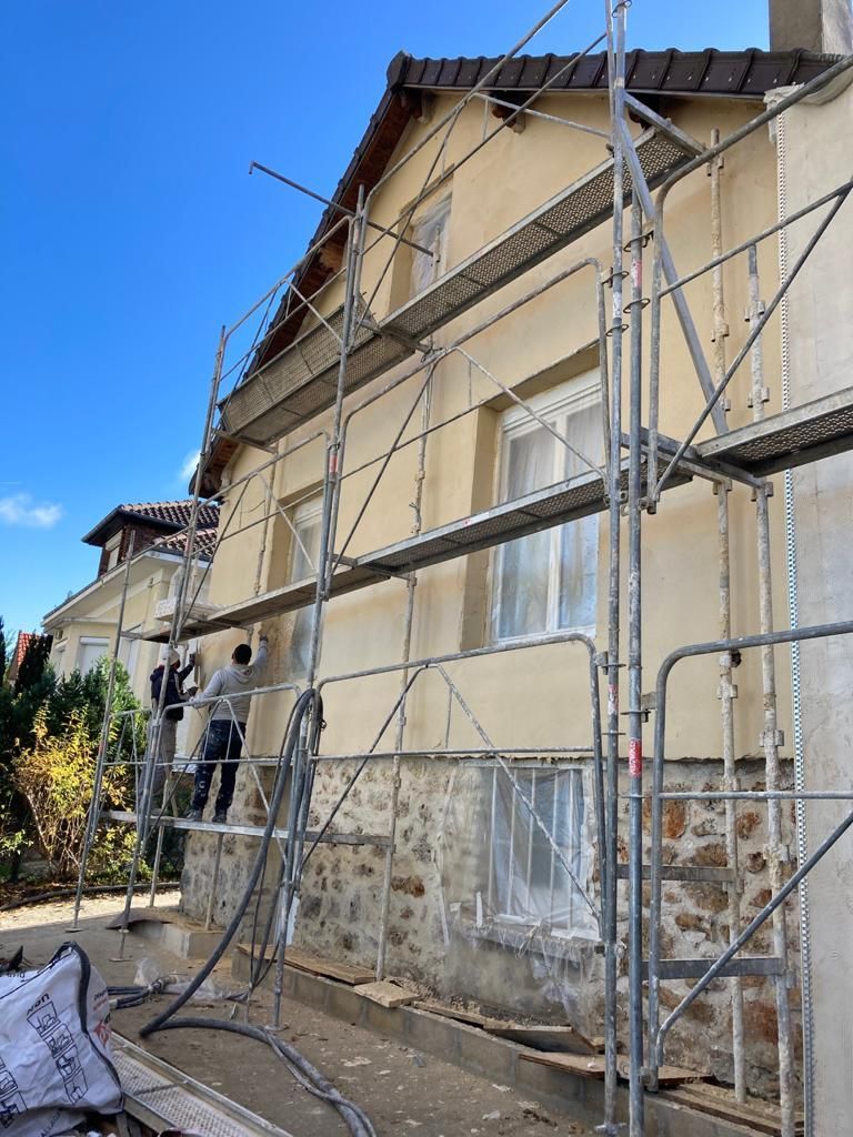Des ouvriers sur des échafaudages appliquent du stuc sur une maison, par une journée ensoleillée.