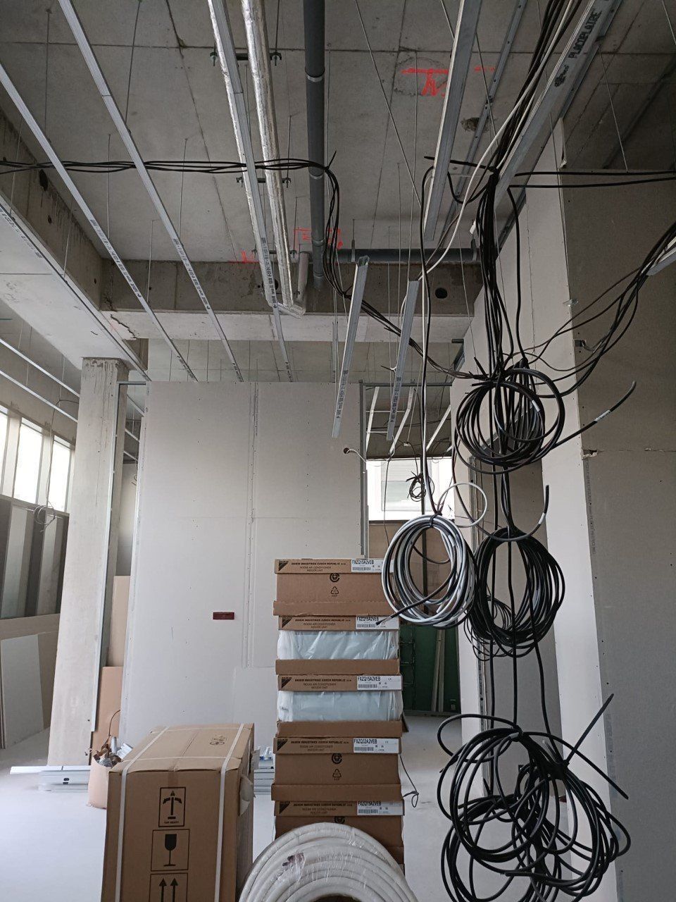 Chantier de construction avec câbles apparents et boîtes électriques empilées contre un mur. Poutres en béton et murs inachevés.