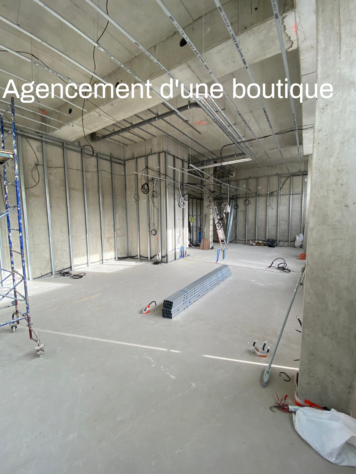 Intérieur d'un magasin en construction avec échafaudages, charpente métallique et câbles électriques apparents.