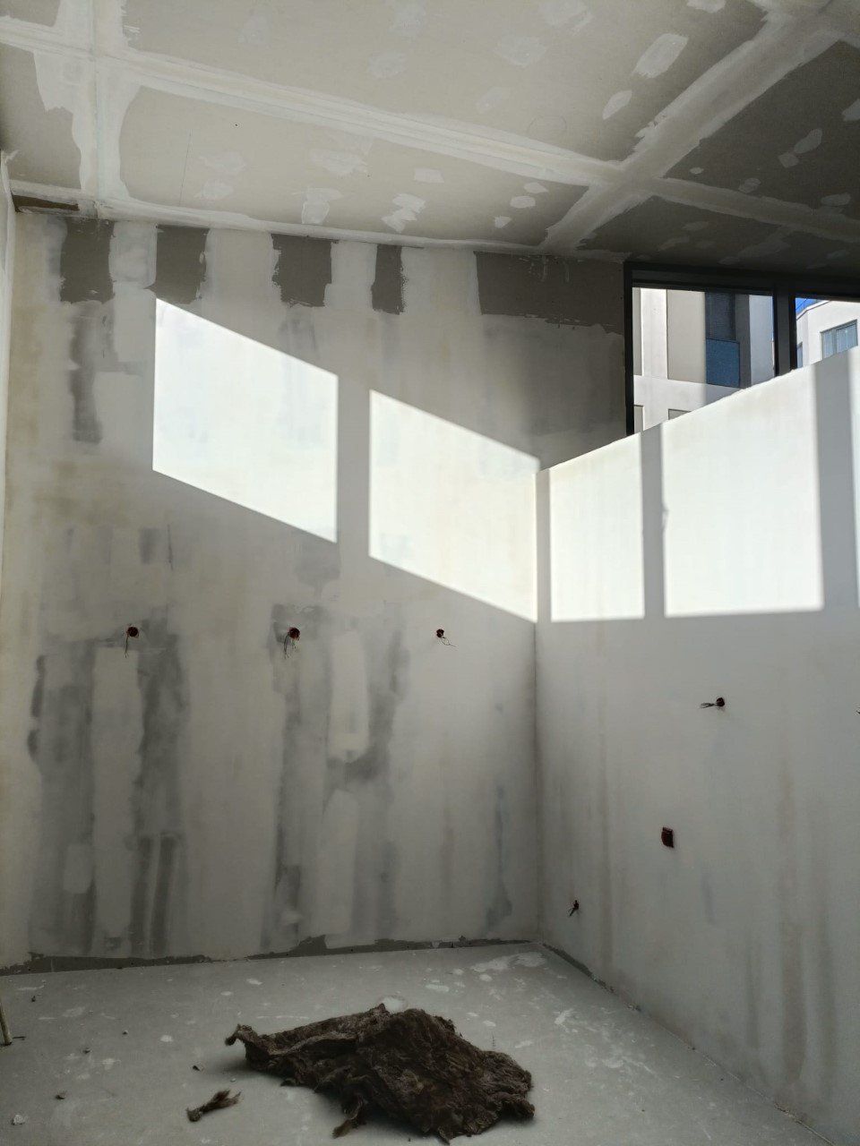 Intérieur d'une pièce en construction, la lumière du soleil filtrant à travers les ouvertures et illuminant les murs et le sol inachevés.