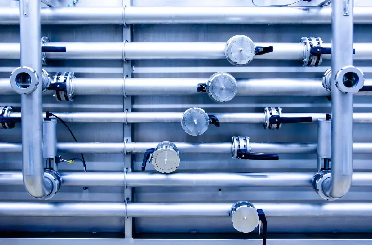 Tuberías plateadas con válvulas contra una pared.