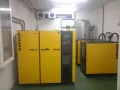 Compresores de aire Kaeser amarillos en un entorno industrial, con un tanque de almacenamiento vertical y tuberías.