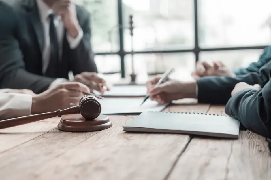 Abogados en una reunión con un mazo, un bloc de notas y documentos sobre una mesa de madera.