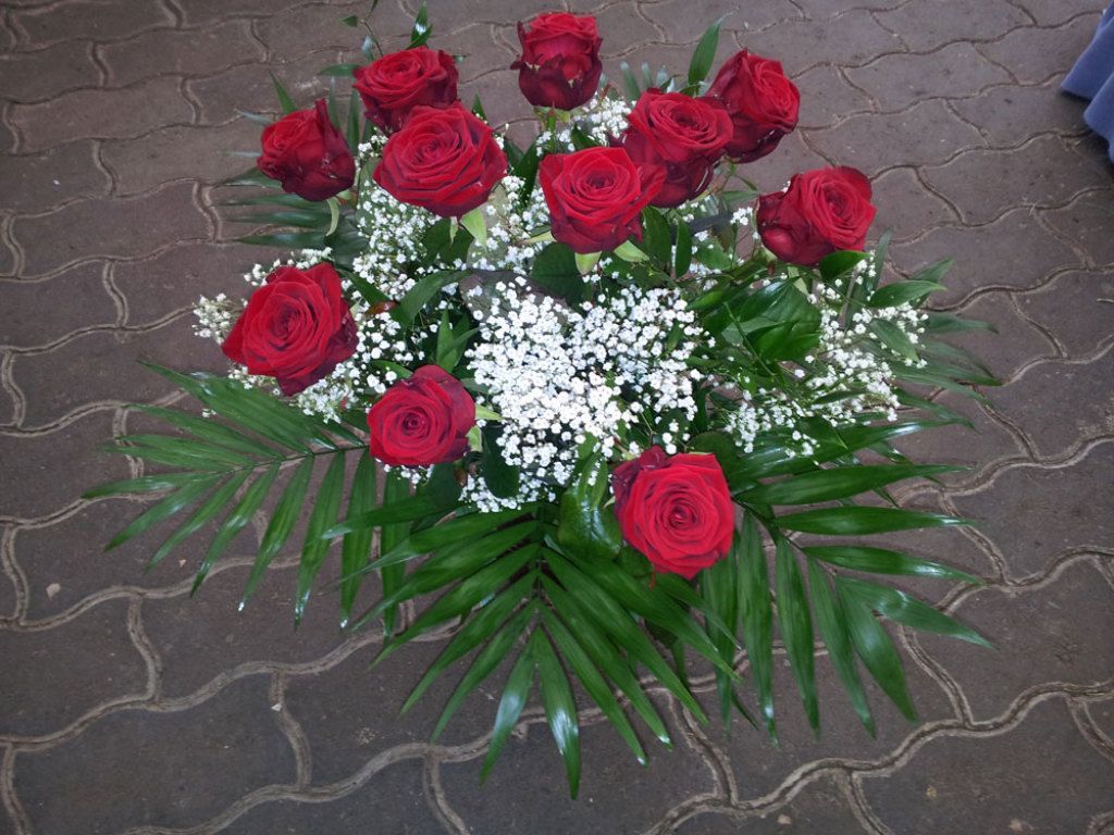 Blumenarrangement aus roten Rosen mit Schleierkraut und grünem Laub auf einer Ziegeloberfläche.