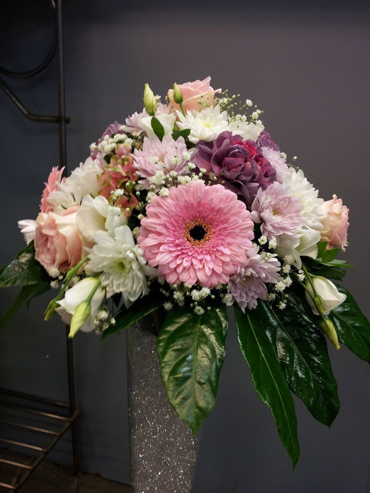 Rosa-weißes Blumenarrangement in einer silbernen Vase mit grünen Blättern vor grauem Hintergrund.