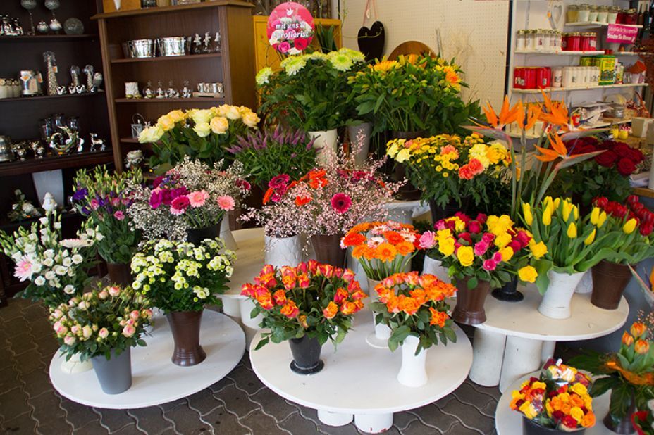 Blumenladen-Auslage: Bunte Sträuße aus Rosen, Tulpen und anderen Blumen, arrangiert auf weißen Tischen.