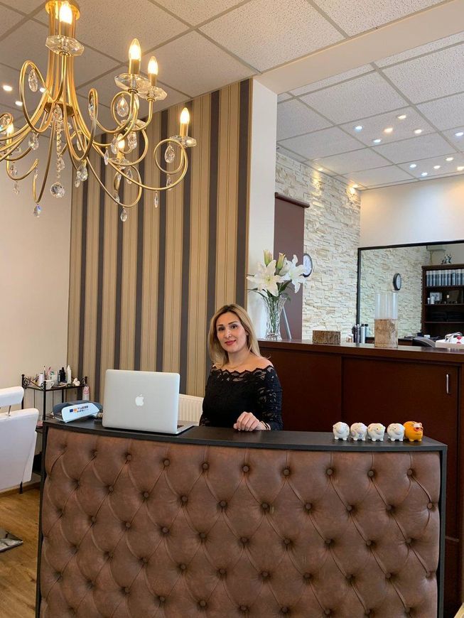 Frau an einem braun gepolsterten Empfangstresen in einem Friseursalon mit Kronleuchter und gestreifter Wand.