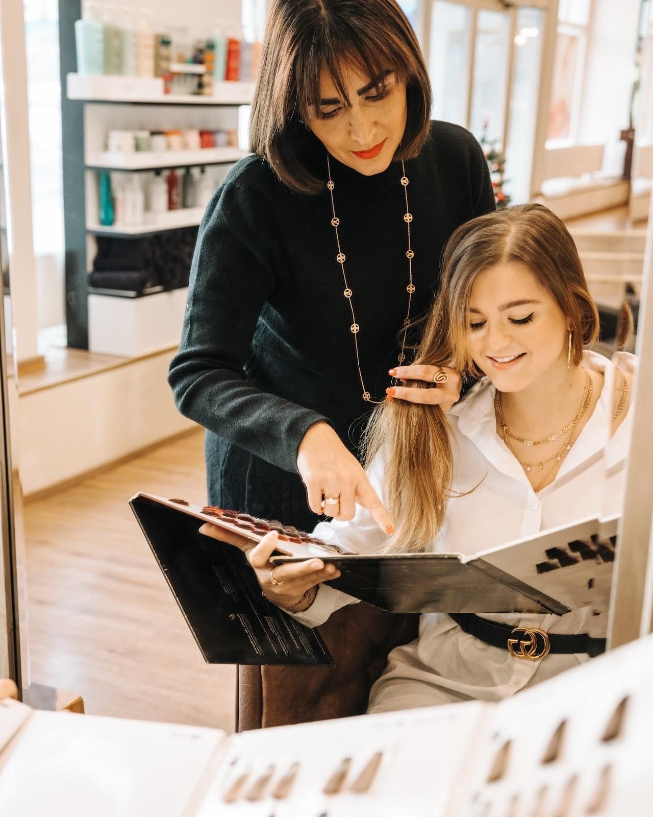 Eine Frau zeigt einer sitzenden Kundin in einem Salon auf Haarfarbmuster.