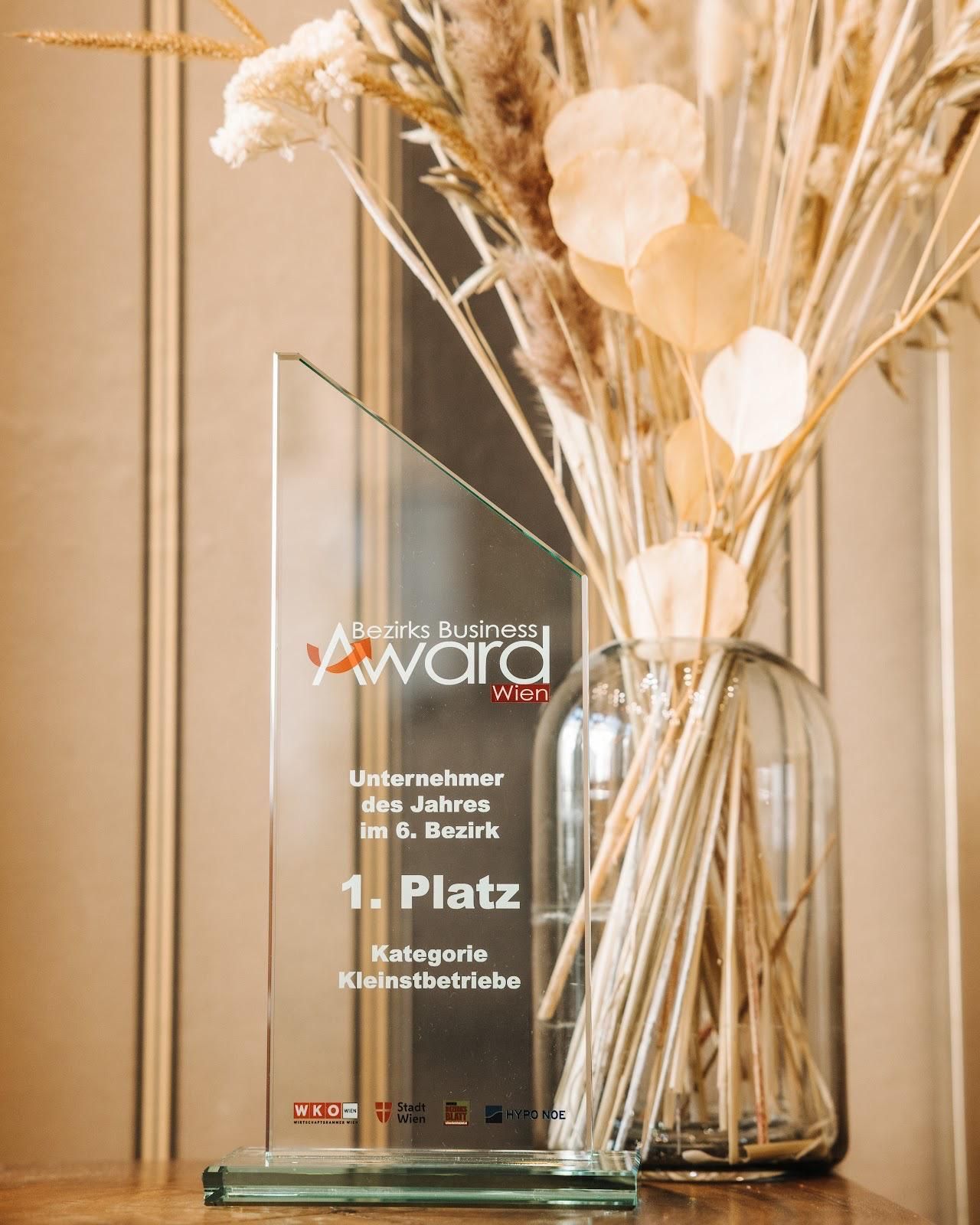 Glas-Firmenpreis mit dem Aufdruck „1. Platz“ neben einer Vase mit Trockenblumen.