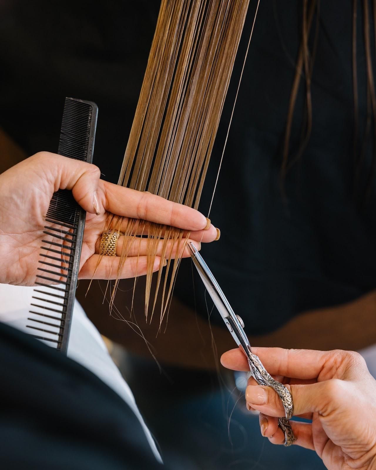 Hände halten Schere und Kamm und schneiden blondes Haar.