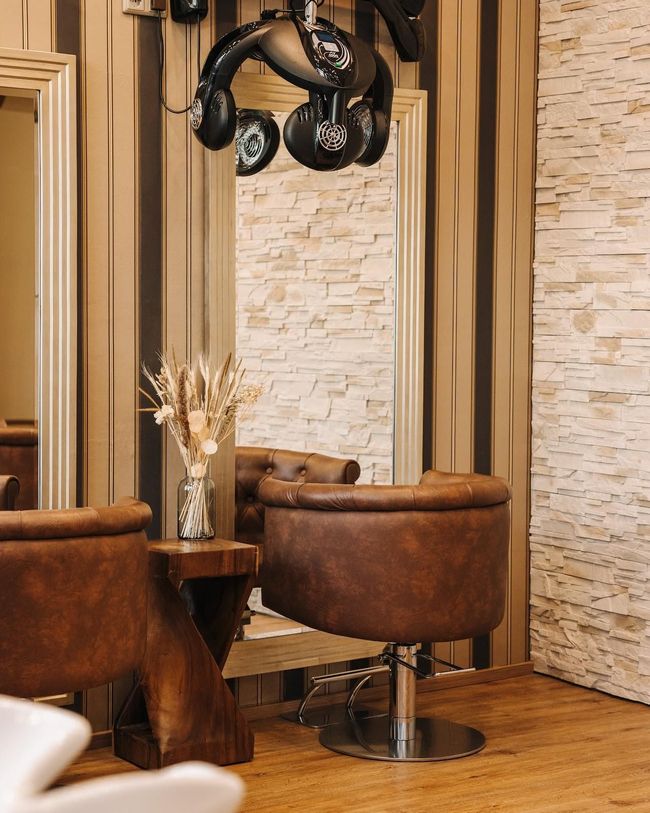 Interieur eines Friseursalons mit braunen Lederstühlen, Spiegel und einem Haartrockner mit Haube im Vintage-Stil.