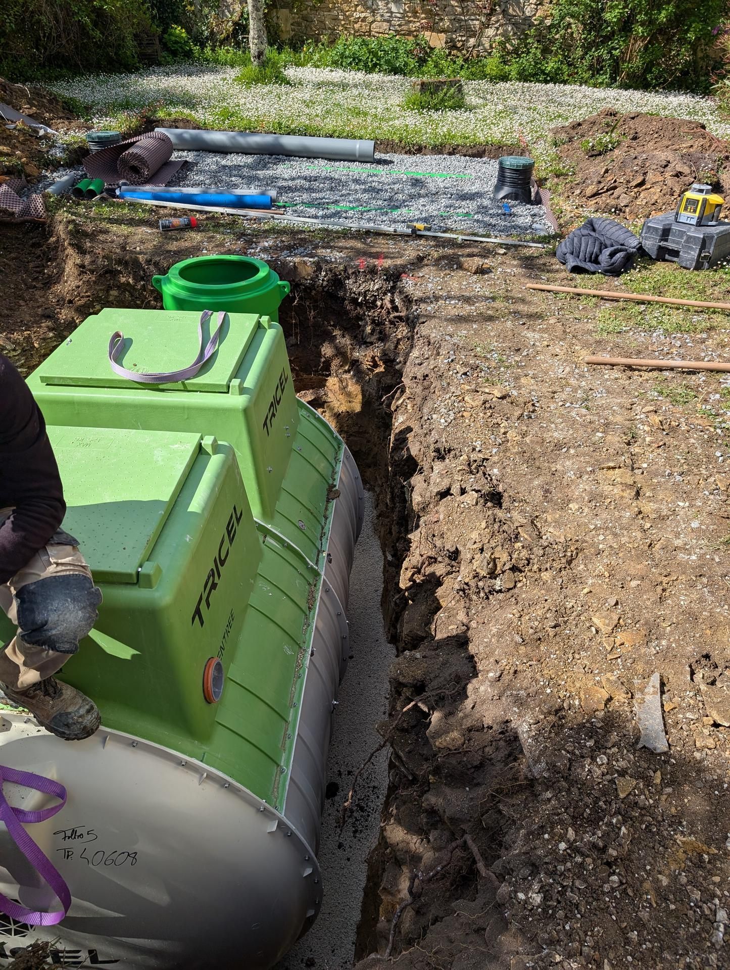 Une fosse septique verte est descendue dans une tranchée étroite ; travaux de construction en cours à l'extérieur.