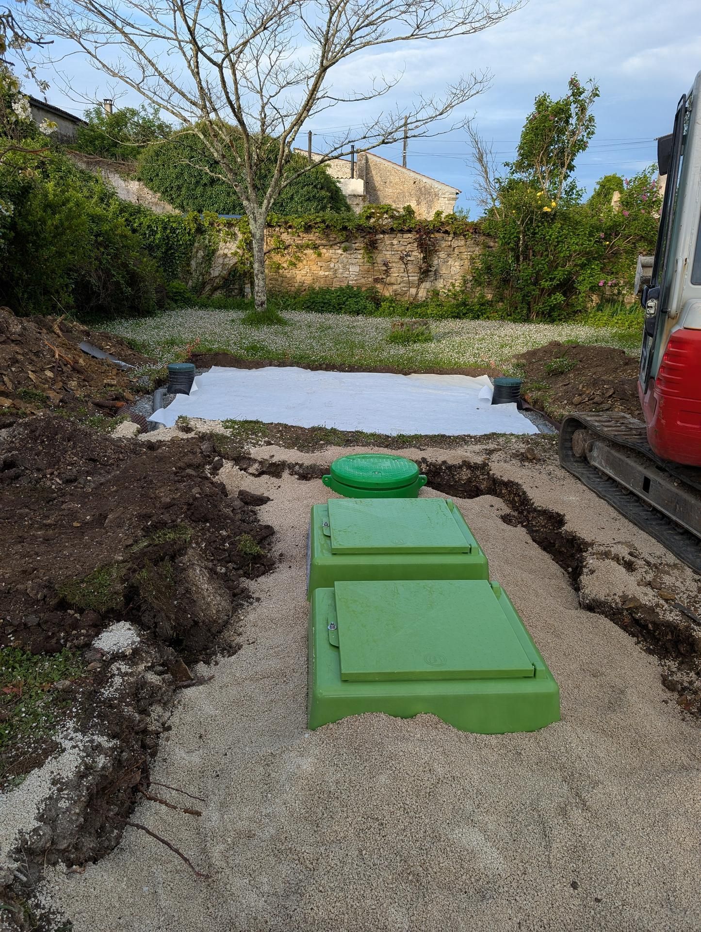 Une fosse septique verte est installée dans une tranchée tapissée de gravier, au sein d'un chantier de construction.