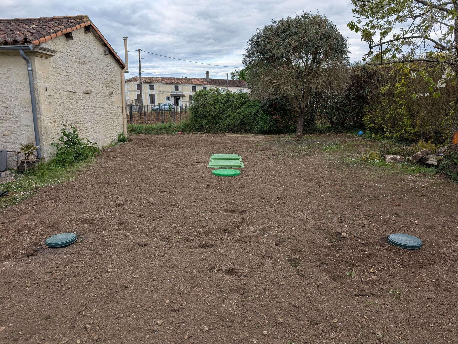 Une cour arrière avec un parterre labouré et deux accès circulaires ; une petite structure verte se trouve au centre.