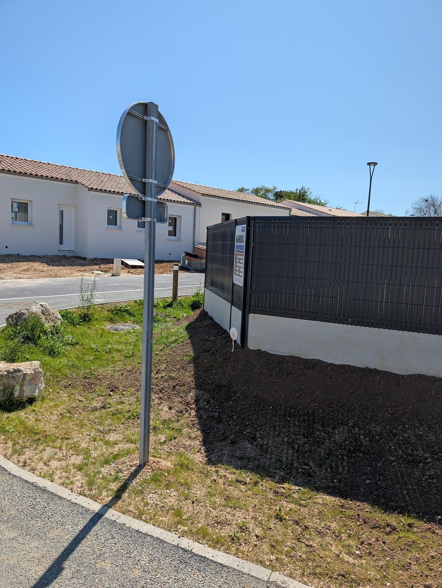 Panneau de rue sur le trottoir, avec des maisons et une clôture sous un ciel bleu.