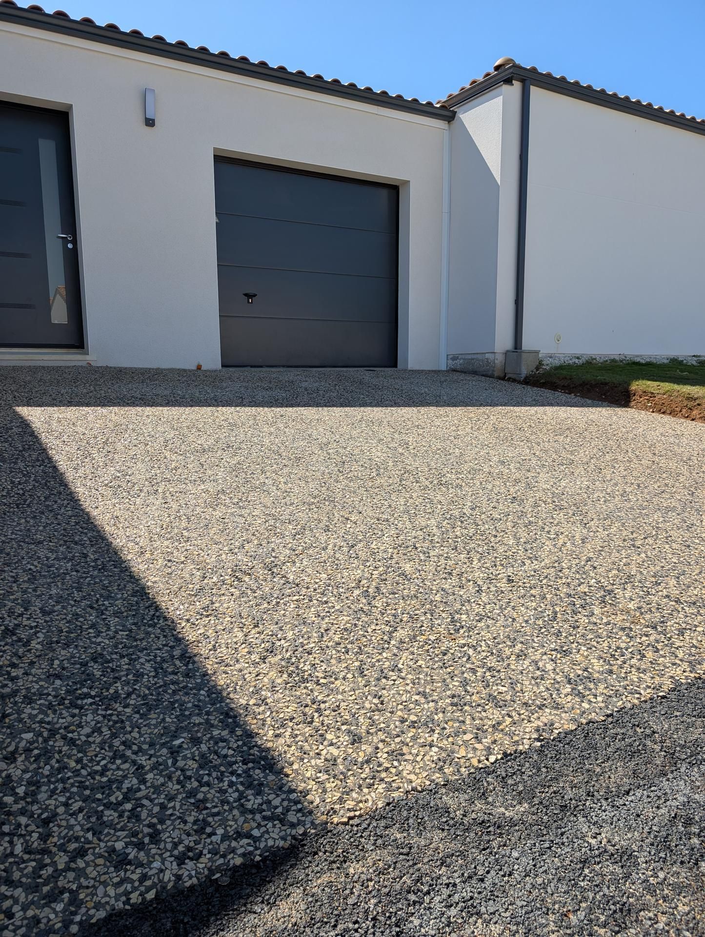 Allée pavée de petits cailloux beiges et gris devant une maison blanche avec garage.