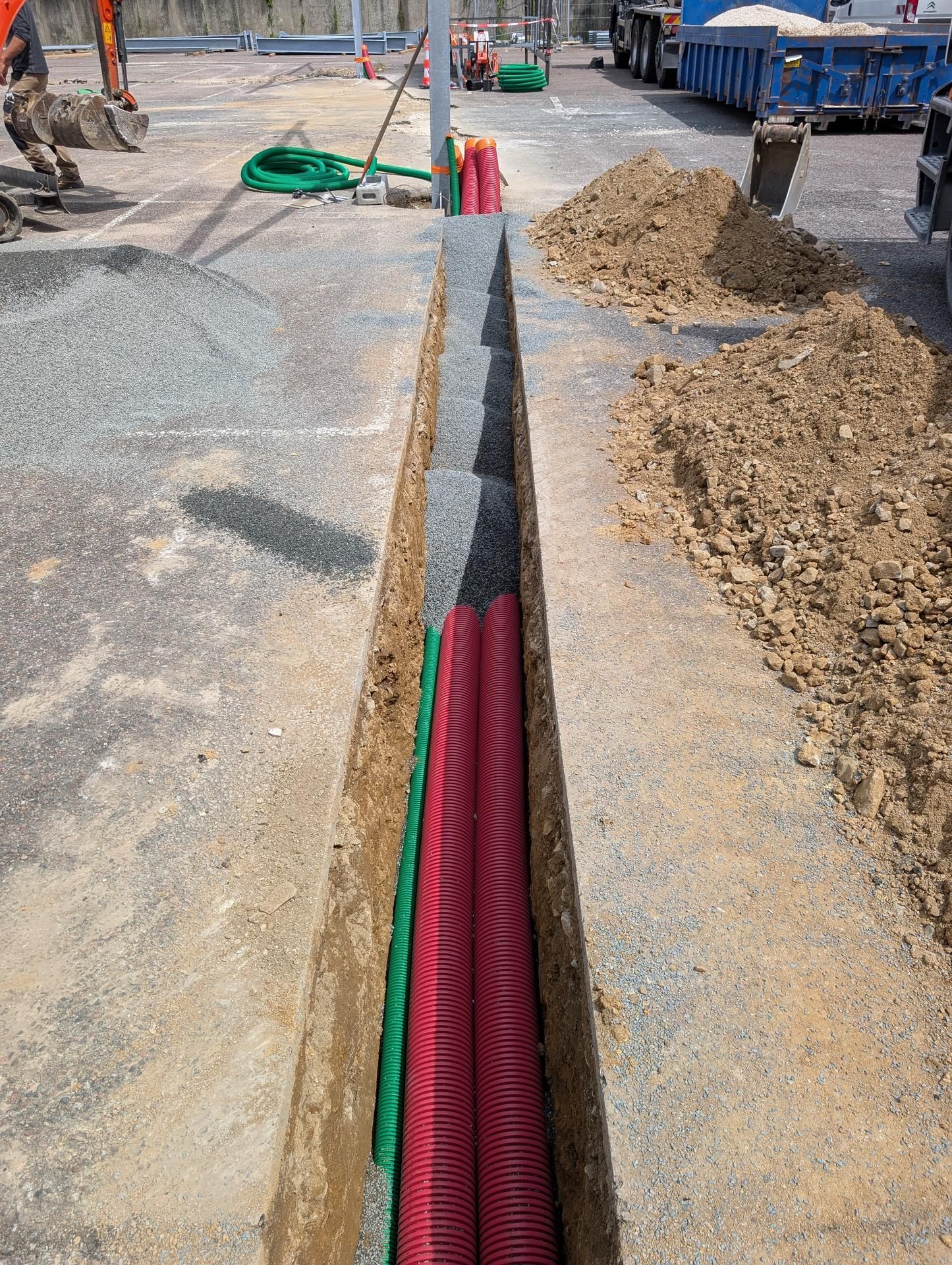 Tranchée creusée dans du béton avec des tuyaux de conduit rouges et verts ; chantier de construction.