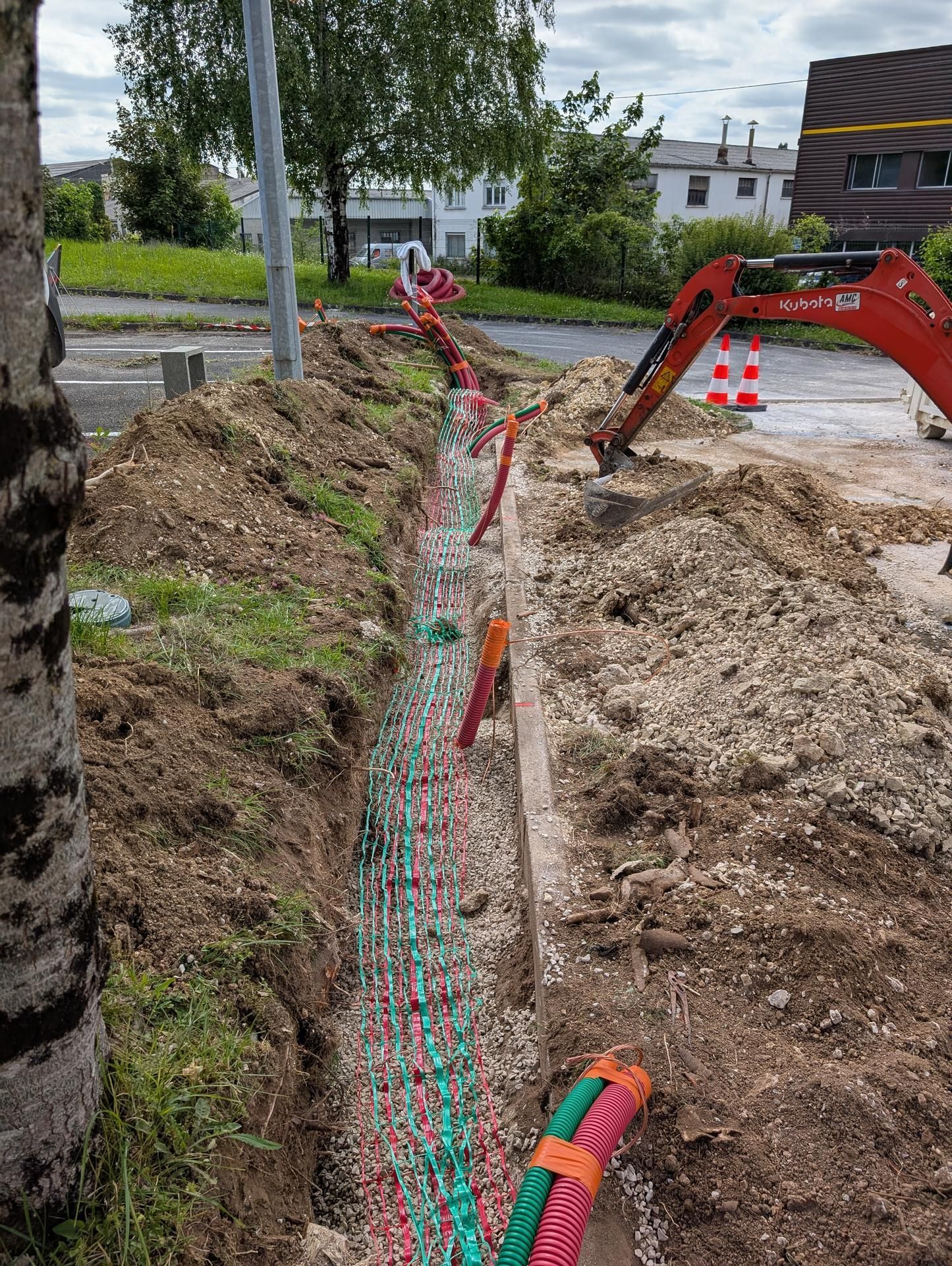 Tranchée creusée dans le sol avec câbles de couleur, excavatrice et chantier de construction.