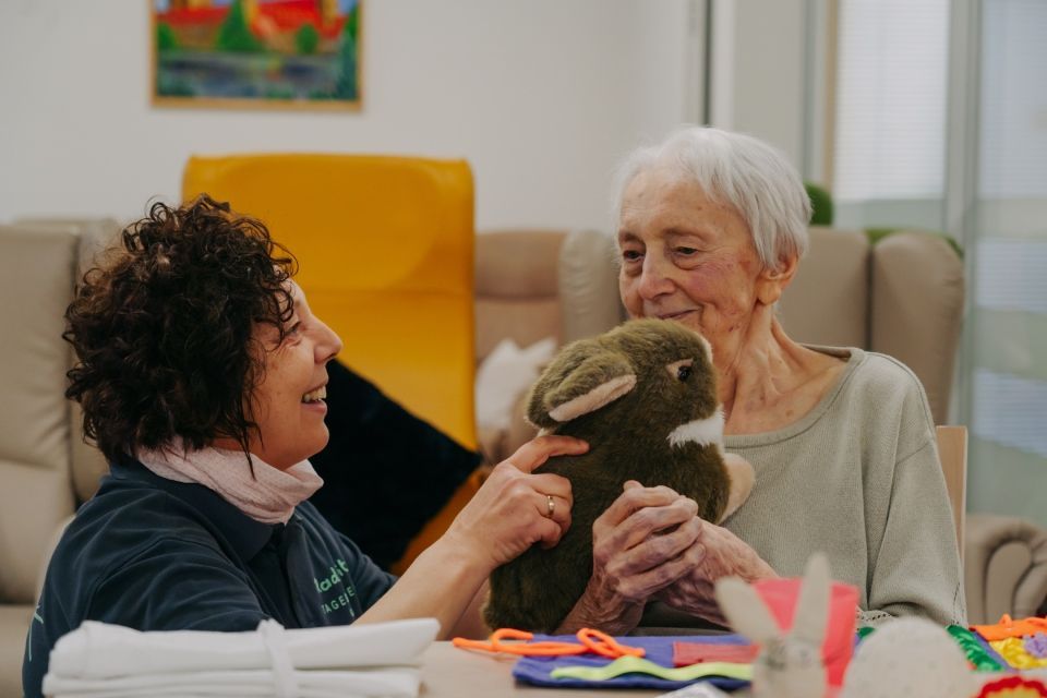 Pflegekraft und älterer Mensch teilen warmen Moment mit Stoffkaninchen gemeinsam