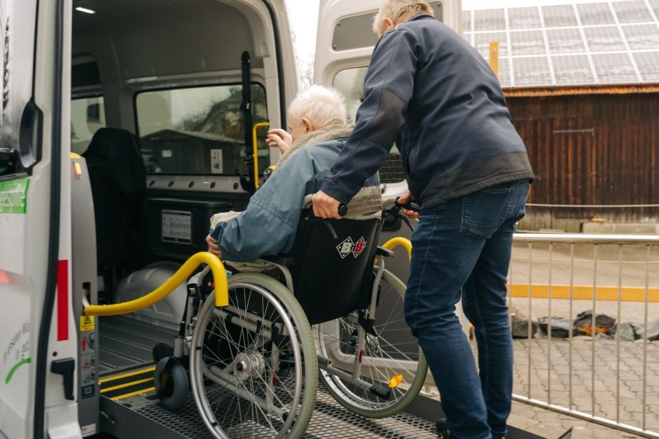 Eine Person hilft einer Person im Rollstuhl auf eine an einem Lieferwagen befestigte Hebebühne.
