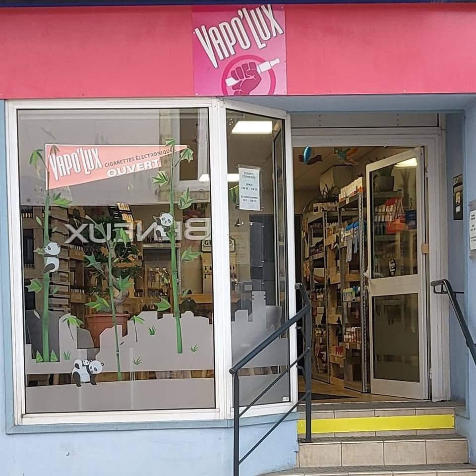 Extérieur de la boutique de vape Vapo'Lux avec porte ouverte. Signalétique rose et blanche. Vitrine ornée de motifs en bambou.