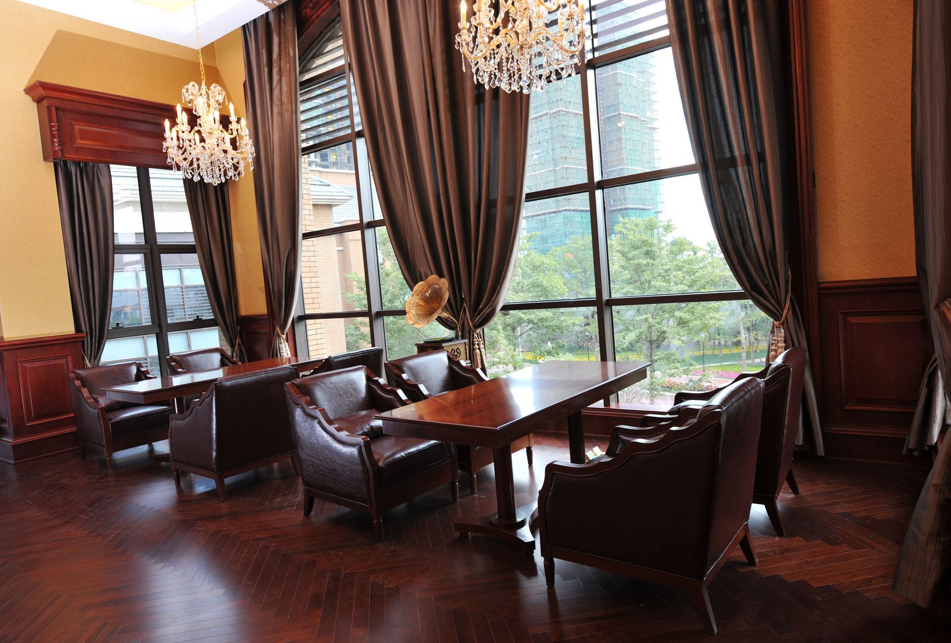 Salon avec table en bois, fauteuils en cuir, lustres en cristal et rideaux marron