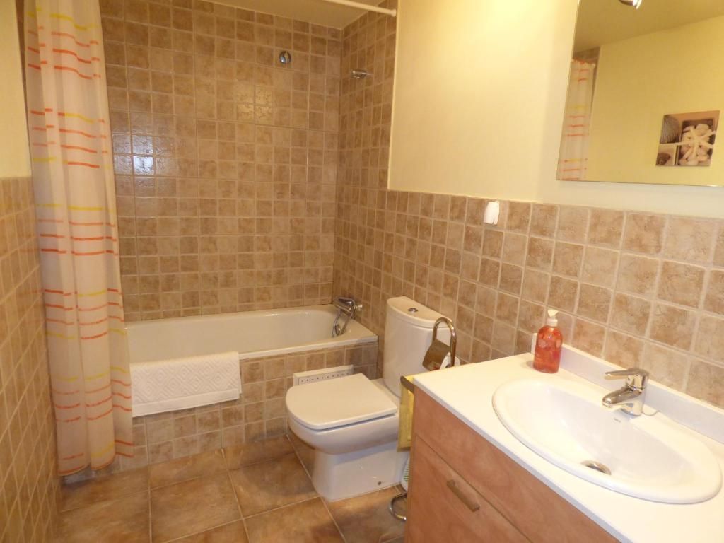 Pequeño baño alicatado con bañera, inodoro y lavabo con mueble en tonos beige.