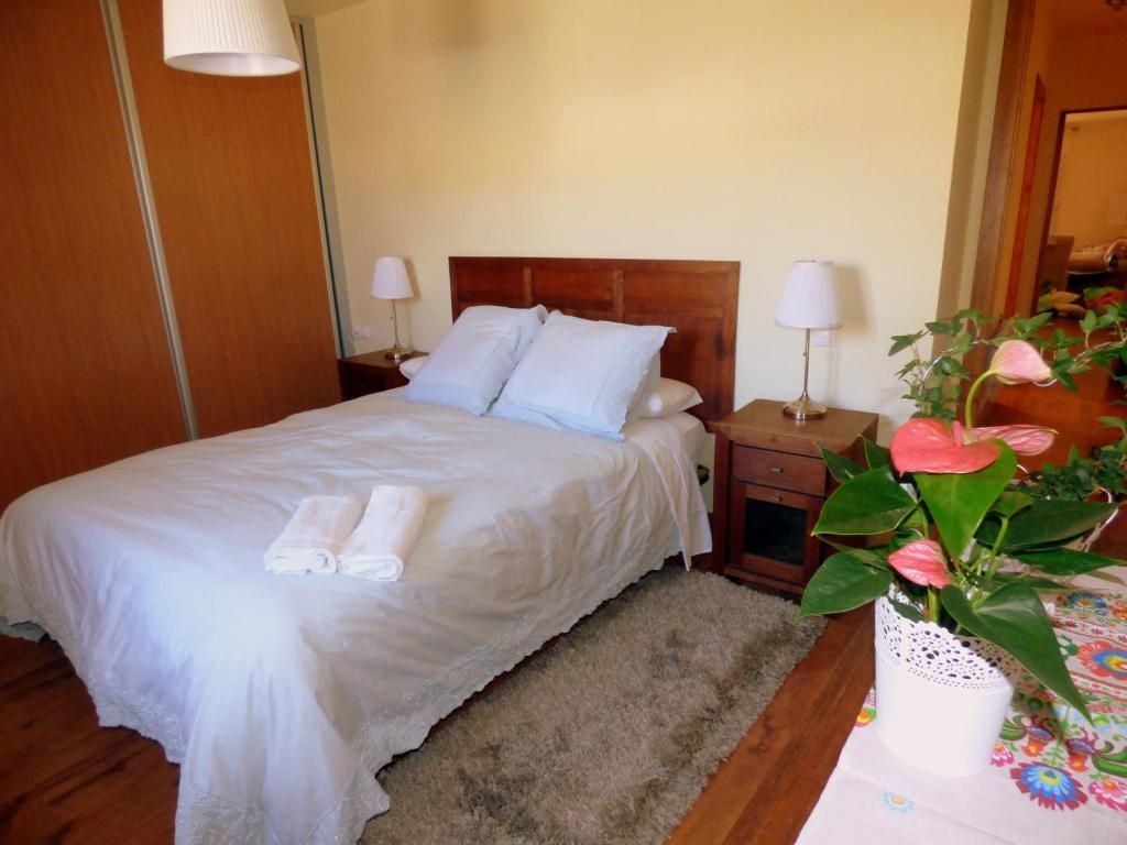 Habitación acogedora con una cama blanca, cabecero de madera, mesitas de noche y una maceta con flores en primer plano.