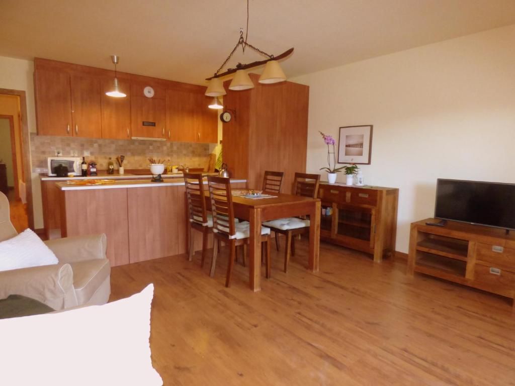 Salón-cocina diáfano con suelos de madera, mesa de comedor, sofá y mueble para la televisión.
