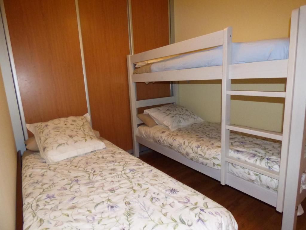 Habitación con una cama individual y una litera blanca, con paredes revestidas de madera y suelo de madera noble.