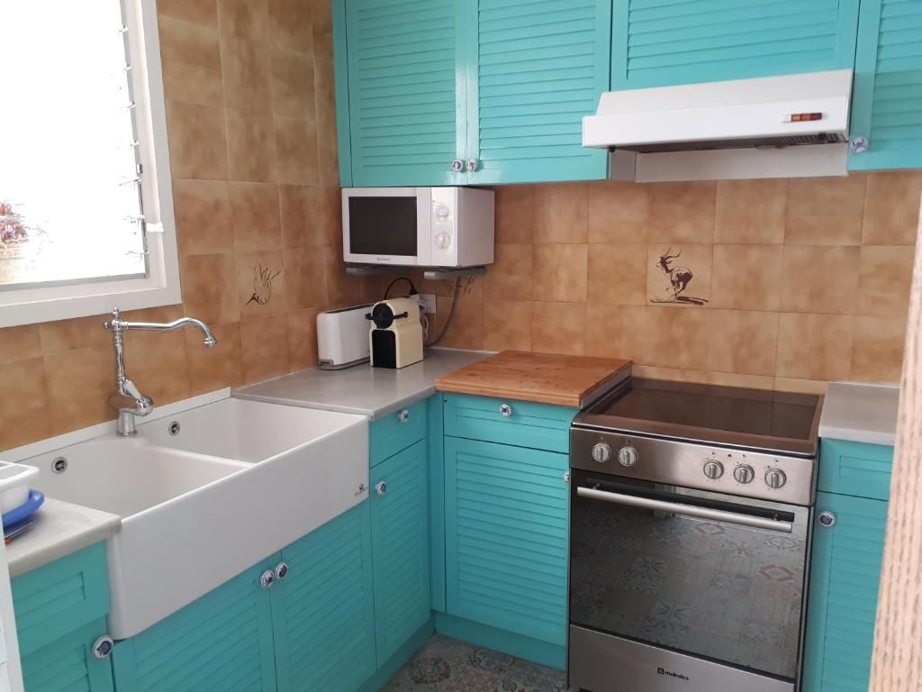Cocina pequeña con armarios turquesa, fregadero blanco, microondas, fogones y paredes alicatadas.
