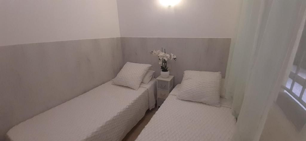 Habitación pequeña con dos camas individuales, sábanas blancas y una mesita de noche con flores.
