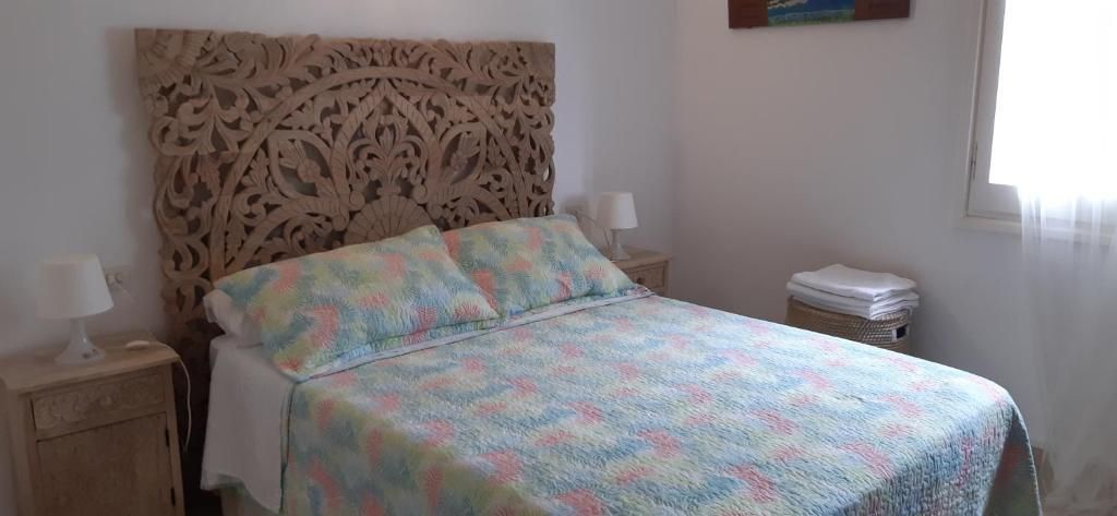 Dormitorio con cabecero de madera tallada, colcha con estampado en tonos pastel, mesitas de noche.