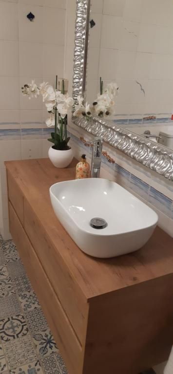 Lavabo moderno con mueble de madera, lavabo blanco y flores decorativas junto a una pared alicatada.