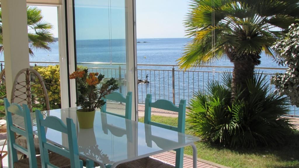 Mesa de comedor de cristal y sillas turquesa con vistas al océano a través de una luminosa ventana del patio.